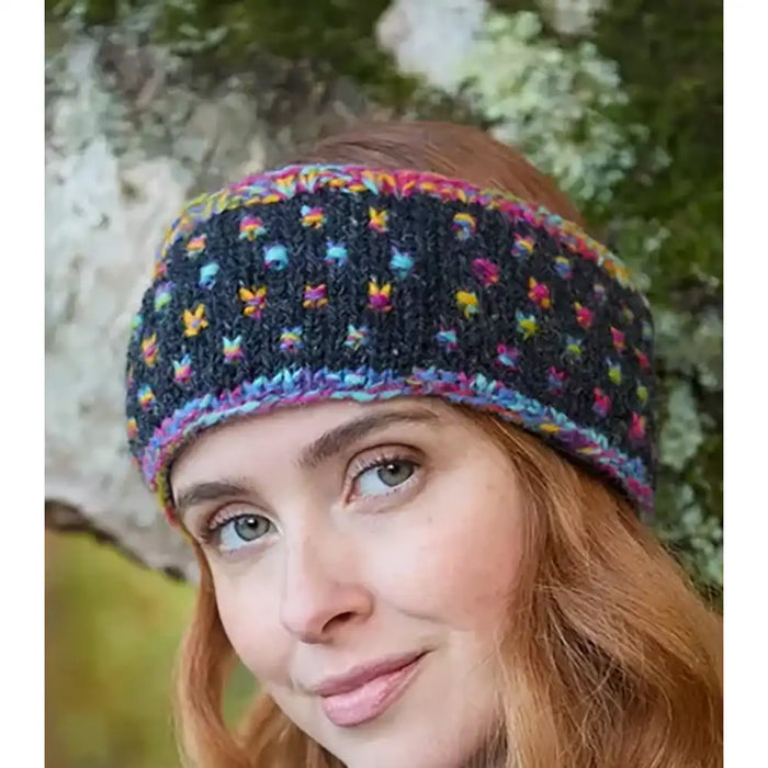 A woman outdoors wearing a dark charcoal knit headband with multicolored patterns and a striped trim.