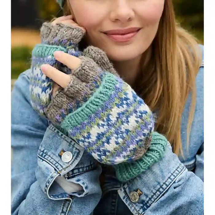 A close-up of a person wearing multicolor knit fingerless gloves with gray cuffs and a blue, green, and white Fair Isle patterned body, paired with a denim jacket.