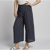 Person wearing black pants with white polka dots on a plain background