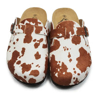 Pair of cow print clogs with brown straps on a white background