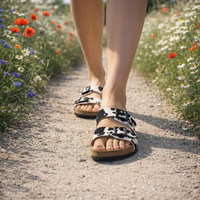 Cow print sandals being worn while walking down a path between wild flowers.