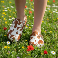 Brown and white cow print shoes on a person standing in a field of flowers.