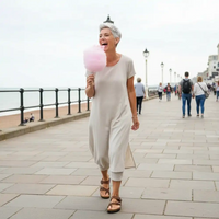 Woman in a light gray jumpsuit holding pink cotton candy on a promenade.