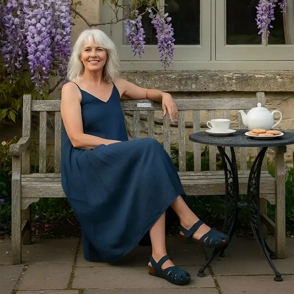 Woman in blue sun dress sat on a bench having tea and biscuits.