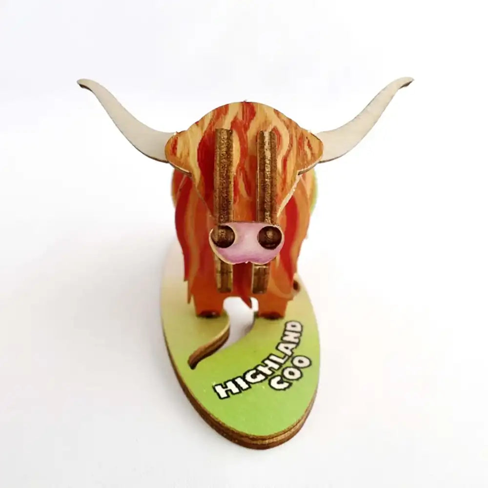 A 3D wooden model of a Highland cow on a light green base labeled 'HIGHLAND COW', photographed against a plain white background.