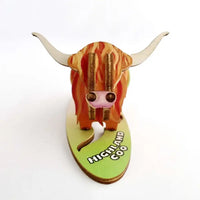 A 3D wooden model of a Highland cow on a light green base labeled 'HIGHLAND COW', photographed against a plain white background.