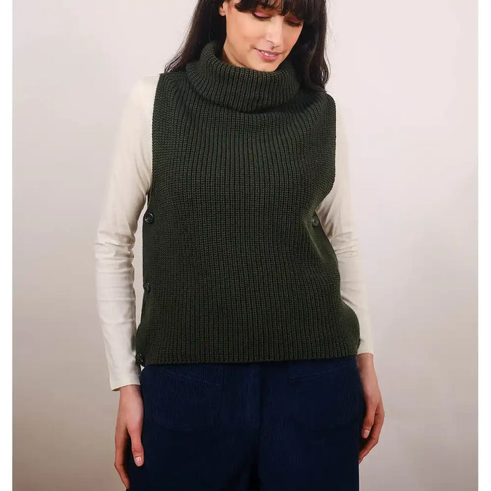 Woman wearing a green knitted vest over a white long-sleeve shirt with a plain background