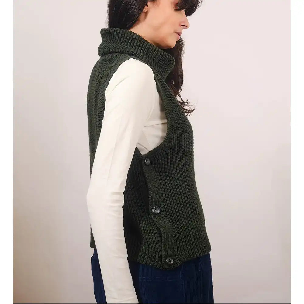 Woman wearing a green knitted vest over a white shirt on a plain background