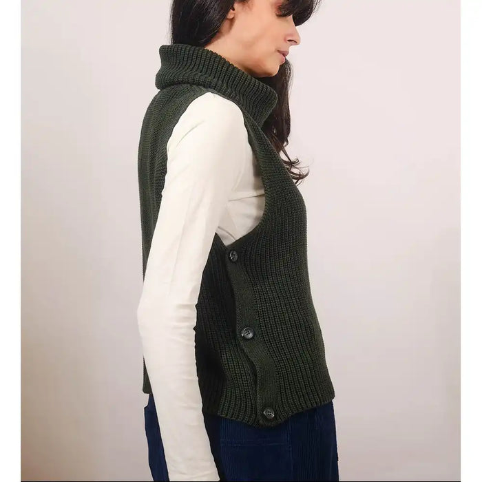 Woman wearing a green knitted vest over a white shirt on a plain background