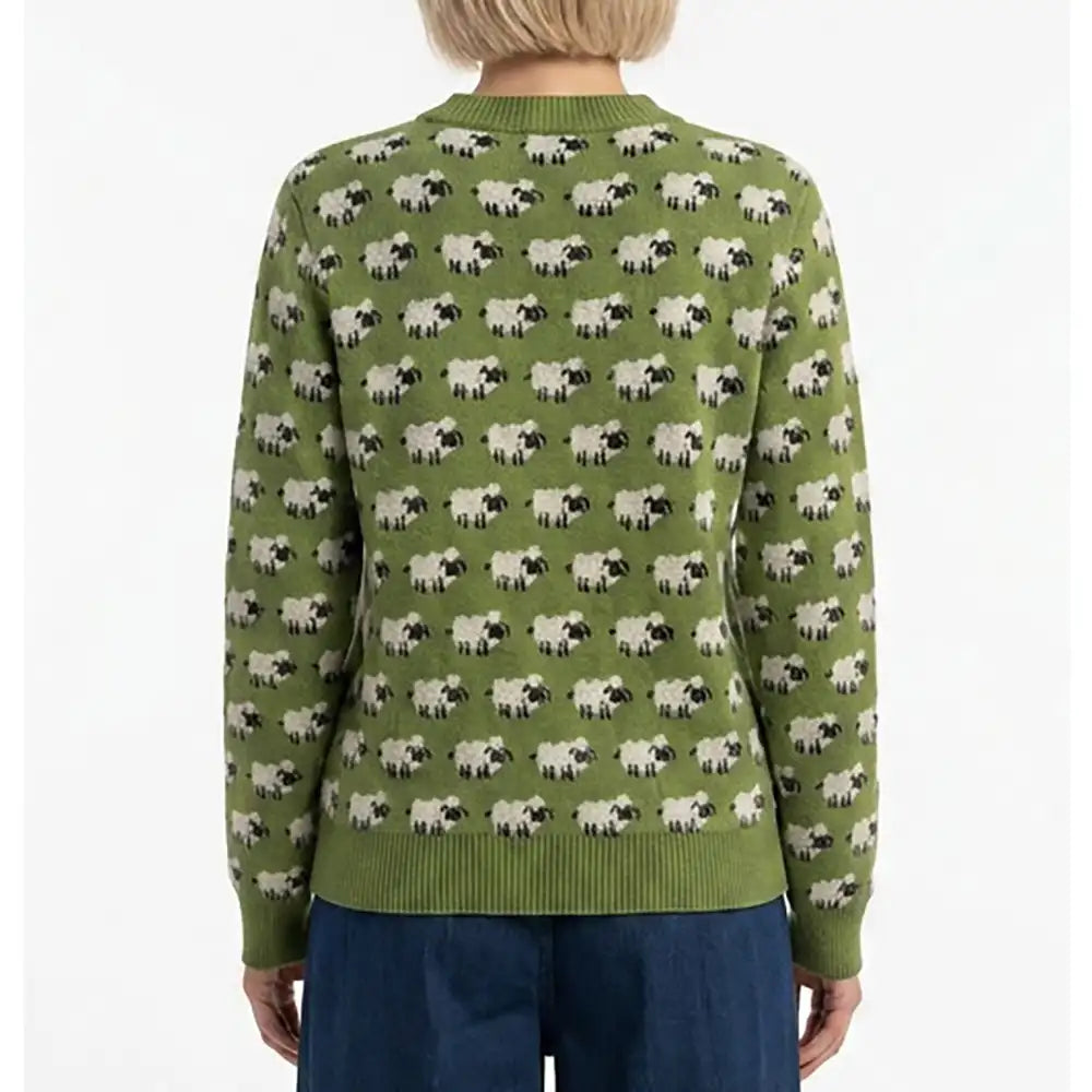 A person shown from the back wearing a green long-sleeve knit sweater with an allover sheep print, paired with dark blue pants, against a plain white background.