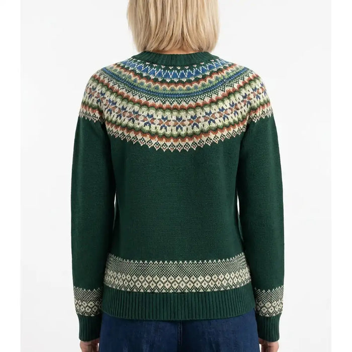 A woman viewed from the back wearing a dark green knit sweater with a multicolor Fair Isle yoke and sleeve cuffs, paired with blue jeans against a plain white background.