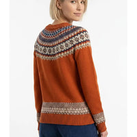 A woman wearing a rust-orange Fair Isle knit sweater with a colorful patterned yoke and cuffs, shown from a three-quarters back view against a white studio background.