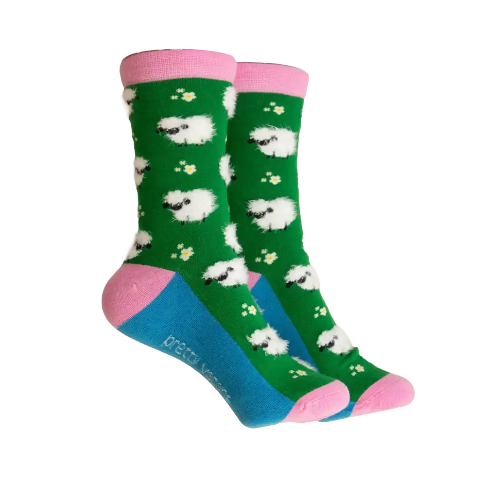 A pair of crew socks with a green background, white sheep pattern, pink cuffs and heels, and a blue toe section. The brand name 'pretty socks' is printed on the side of the blue toe area.