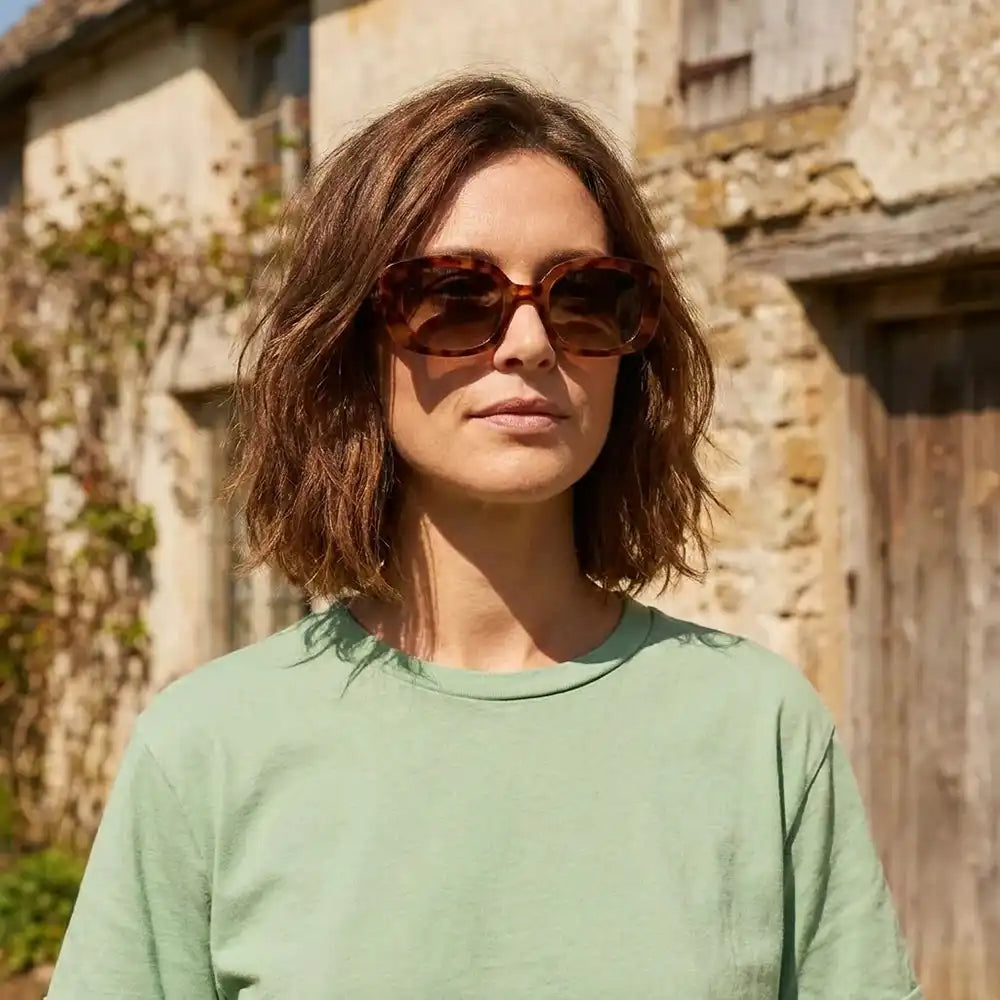 Woman wearing sunglasses and a green shirt in front of a stone building
