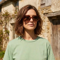 Woman wearing sunglasses and a green shirt in front of a stone building
