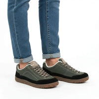 A person wearing cuffed blue jeans and low-top sneakers in olive green, black, and brown, photographed against a clean white studio background.