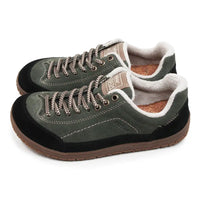 A pair of low-top casual shoes in dark olive green suede and black fabric, featuring brown braided laces, a brown outsole, and a white sherpa lining.