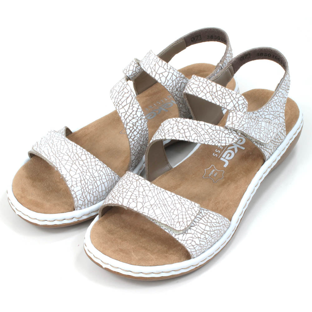 Rieker flat strappy sandals in white with cracked effect. Velcro fitting and adjustment. Tan coloured insoles. Angled view.AC