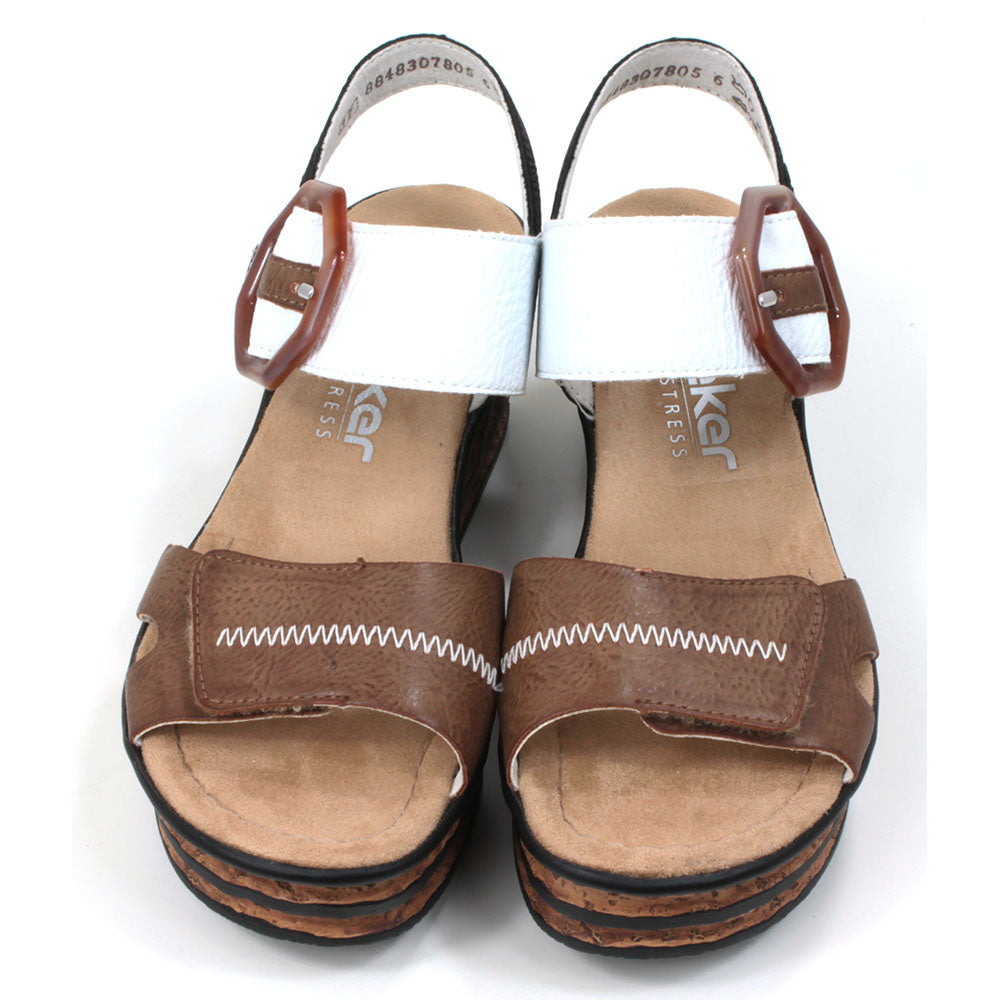 Rieker cork wedge sandals. Velcro fitting and adjustment. Brown over toes strap. White over upper foot strap with brown buckle detail. Black strap around the ankle. Tan insoles. Front view.