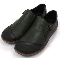 Pair of dark green leather shoes with zips on a white background. Angled view.