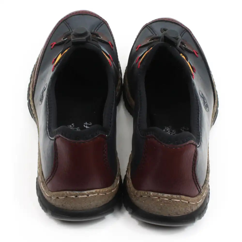 Rieker dark blue leisure shoes. Black fabric padding around the ankle and over the top of the tongue. Blue, yellow and brown details around the first,third and fifth lace eyes. Burgundy panels around the shoe backs.  Fastens with elastic laces which are adjusted with a push button gripper. Cork and black rubber soles. Back view.