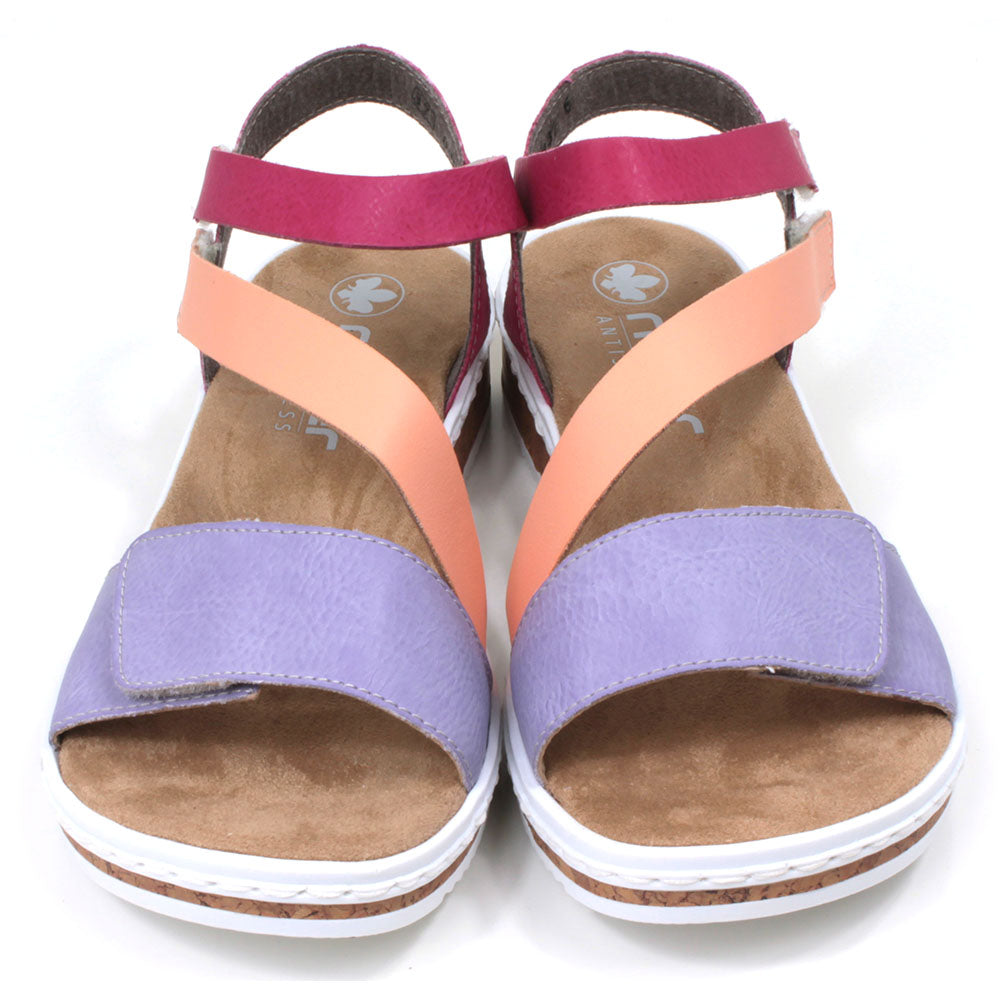 Rieker sandals with sand coloured footbed. Violet, orange and rose pink straps which adjust and fit with Velcro. Soles have white edging. Front view.