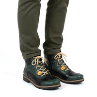 A pair of dark green and black lace-up boots with tan laces and a small orange accent, worn with olive green pants against a white background.