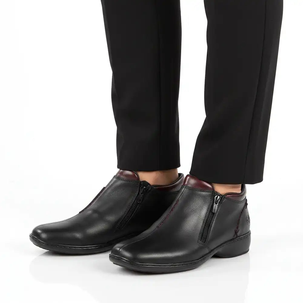 Black leather ankle boots with side zippers, shown on a model wearing black trousers against a white studio background.