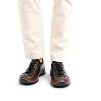 A person wearing off-white trousers and dark brown leather lace-up shoes with black soles, shown from the knees down on a white studio background.