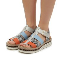 A pair of women's platform sandals with a mix of metallic silver straps, light blue straps, orange straps, and black-and-white leopard print panels, shown on a model's feet against a white background.
