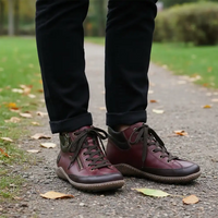 A person standing on a gravel path outdoors wearing dark burgundy leather lace-up ankle boots with dark brown laces and black pants.