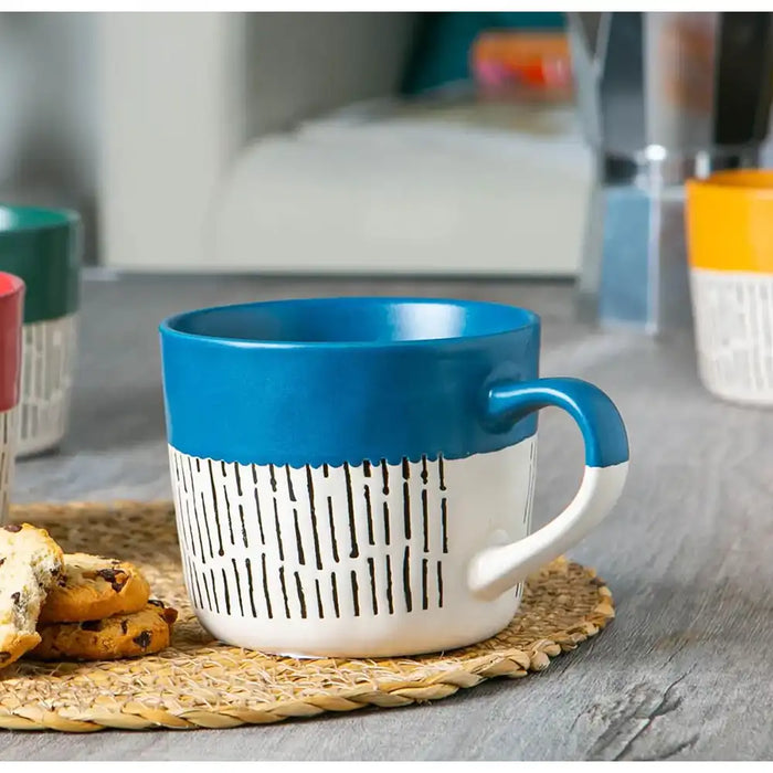 Blue and white mug with a textured design on a woven coaster, blurred background