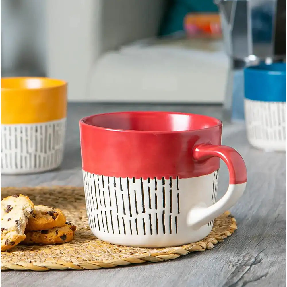 Red and white mug with a textured design on a woven mat, with cookies and another mug in the background.
