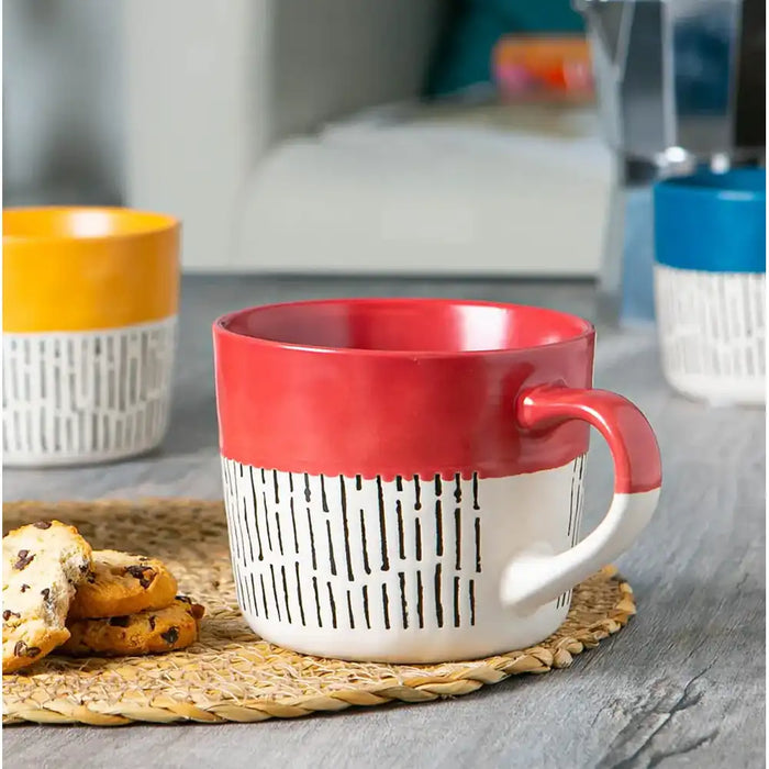 Red and white mug with a textured design on a woven mat, with cookies and another mug in the background.