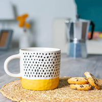 Patterned mug with a yellow base on a woven mat, with cookies nearby.