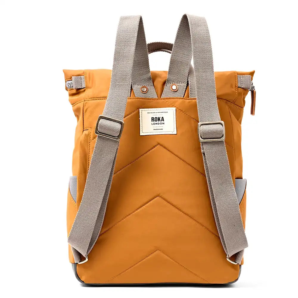 Back view of a caramel backpack with grey webbed shoulder straps and a white brand label reading 'ROKA' In the centre, shown against a plain white background.