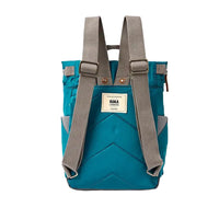 Back view of a teal blue ROKA brand backpack with grey adjustable shoulder straps and a cream-colored brand label in the centre, shown against a plain white background.