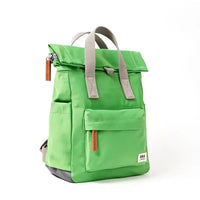 Side view of a dark lime backpack with roll top and front pocket with ROKA label in white on bottom right corner and a slip pocket on the side.