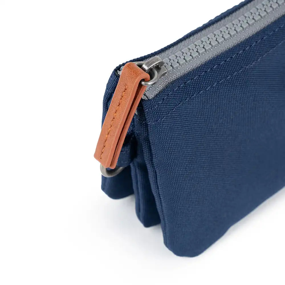 Close-up of a blue purse with a grey zipper and brown leather pull tab on a white background