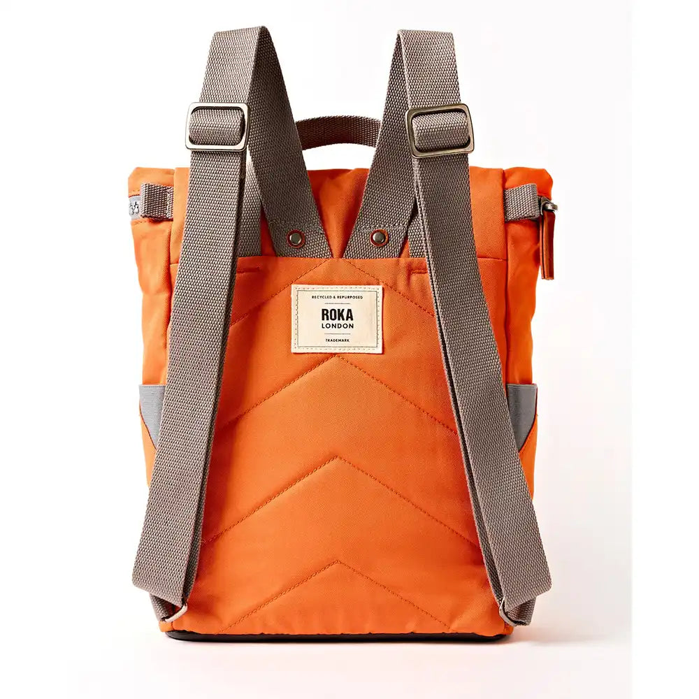 A back view of an orange quilted canvas backpack with dark grey adjustable shoulder straps and a white brand label on the front, shown against a plain white background.