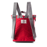The back of a red canvas backpack with grey webbed shoulder straps and a logo label, shown against a plain white background.