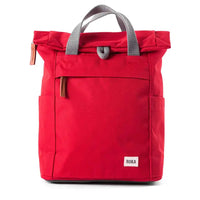 A red roll-top backpack with grey webbed handles, side pockets, and a small white ROKA brand label on the lower front, photographed on a clean white background.
