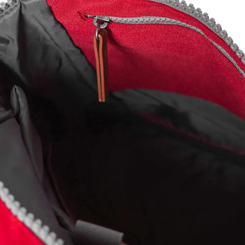 Close-up of the interior of a red backpack, showing a black padded lining, a red fabric upper section, grey zipper trim, and a brown zipper pull tab.