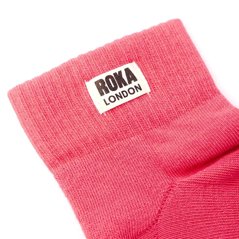 Close-up of a pink sock with a Roka London label on a white background
