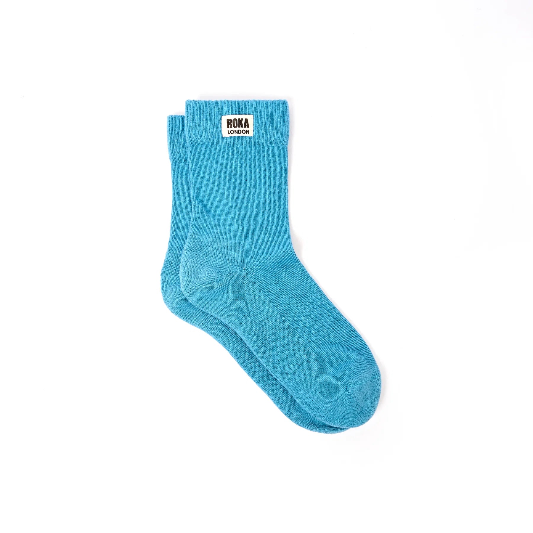 A pair of bright turquoise blue crew socks with a white brand label reading 'ROKA LONDON' on the cuff, displayed on a clean white background.