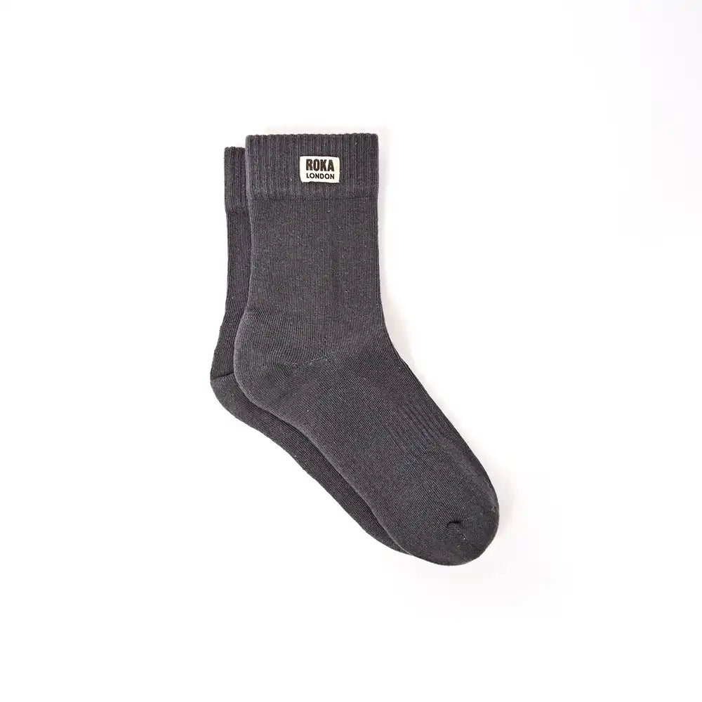 A pair of faded black crew socks with a small white brand label reading 'ROKA LONDON' on the cuff, shown against a plain white background.