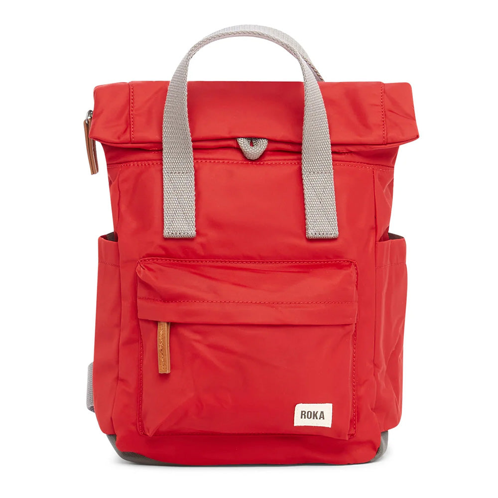 Front view of a cranberry red backpack with roll top and front pocket with ROKA label in white on bottom right corner.