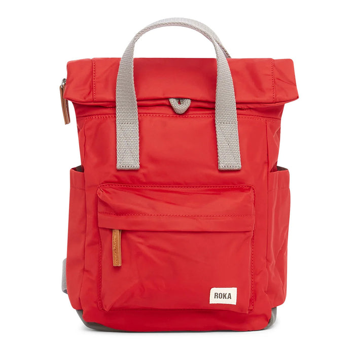 Front view of a cranberry red backpack with roll top and front pocket with ROKA label in white on bottom right corner.