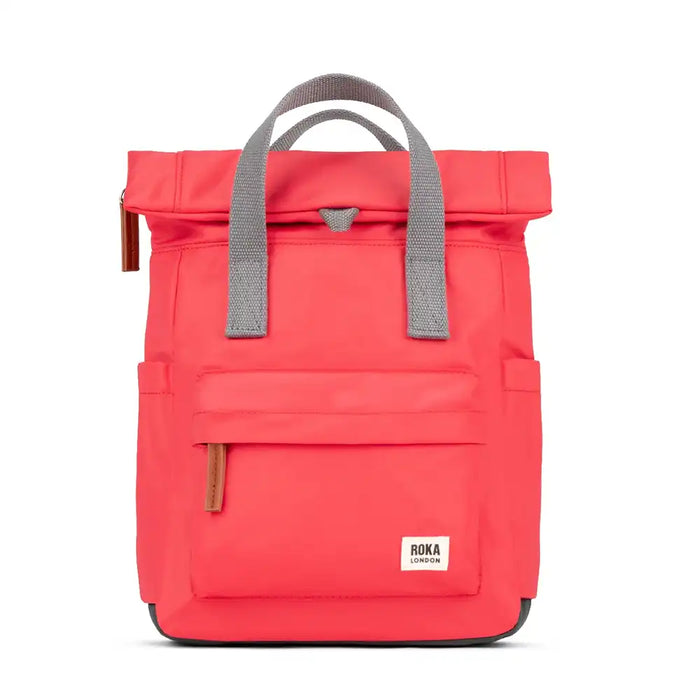 Vibrant poppy pink backpack with a roll top, canvas grey carry handles and side pockets. Front zip fastening pocket with a tan brown zip pull and Roka London logo. 