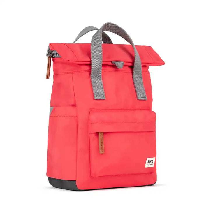 Side of a vibrant poppy pink 
backpack, grey canvas carry handles and side pockets. Front pocket with a zip pull in tan brown and Roka London logo. 
